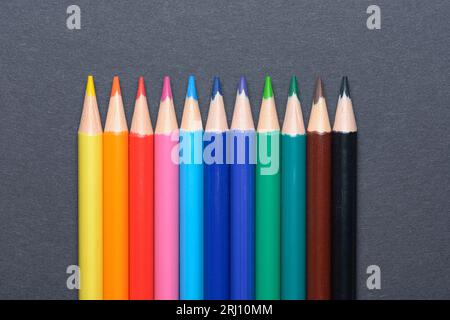 Sammlung von farbigen Buntstiften, die in einer Reihe angeordnet sind, Kunst- oder Zeichenausrüstung auf dunklem Hintergrund Stockfoto
