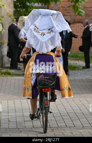 Burg, Deutschland. August 2023. Eine Frau aus der Heimat und Trachtenverein in Burg im Spreewald kommt auf ihrem Fahrrad in sorbisch-wenischer Tracht in den Dienst. Am Nachmittag findet die große Parade zum 29. Heimat- und Trachtenfest im Spreewald statt. Quelle: Patrick Pleul/dpa/Alamy Live News Stockfoto