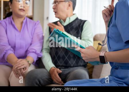 Pflegekräfte sitzen auf dem Sofa Check-up und diagnostizieren mit älteren Paarpatienten über die Gesundheit im Wohnzimmer zu Hause, Hausmeister sitzt auf Couch Erklären Stockfoto