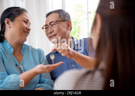 Immobilienmaklerin Frau, die Schlüsselform Haus mit Glück mit älteren Ehepaar zu Hause gibt, Immobilienmakler oder Berater geben Schlüssel der Immobilie mit Familie f Stockfoto