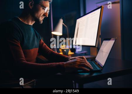 Kaukasischer Mann, der spät nachts in seinem Heimbüro arbeitet, mit einem Laptop an einem Projekt beteiligt war. Geschäftsmann, der Technologie nutzt, um außerhalb der Geschäftszeiten zu arbeiten Stockfoto