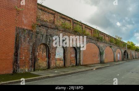 Eine Linie aus gemauerten Bögen, die eine Eisenbahnlinie stützen, die entlang einer verlassenen Straße verläuft. Stockfoto