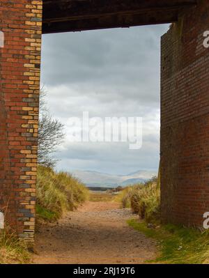 Der Blick unter einer alten Backsteinbrücke auf einen Strand mit den Lake District Gipfeln ist in der Ferne leicht sichtbar. Stockfoto