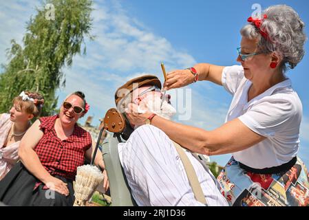 Burg, Deutschland. August 2023. Eine Frau rasiert einen Mann während des Festes in der Spreewaldstadt Burg. Am Nachmittag fand die große Parade zum 29. Heimat- und Trachtenfest im Spreewald statt. Quelle: Patrick Pleul/dpa/Alamy Live News Stockfoto
