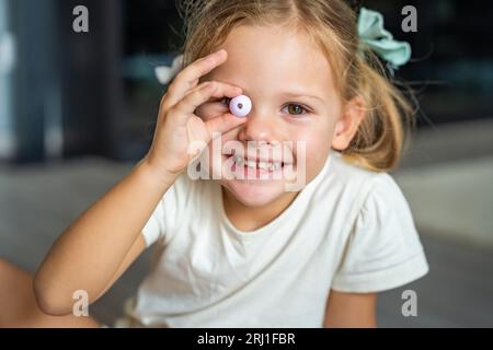 Das kleine Mädchen spielt mit Perlen, die ein Armband aus Holzperlen herstellen. Kindliche Kreativität und Entwicklung feinmotorischer Fähigkeiten Stockfoto