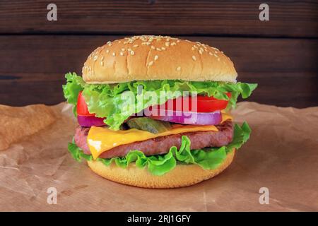 Hamburger oder Burger mit Hackfleisch, Käse, Salat, Tomaten, Zwiebeln, Gurken und Brötchen mit Sesamsamen. Leckeres, farbenfrohes Sandwich auf dem Stockfoto