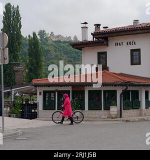 Frau in roter traditioneller Kleidung mit Fahrrad vor dem Restaurant Inat Kuca in Sarajevo, Bosnien und Herzegowina, 19. August 2023. Stockfoto