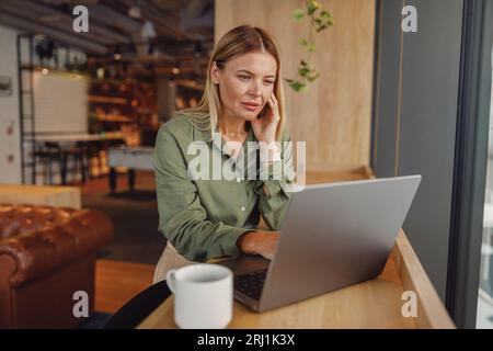 Fokussierte Unternehmerin, die an einem Laptop arbeitet, in moderner Zusammenarbeit. Entfernungsarbeitskonzept Stockfoto