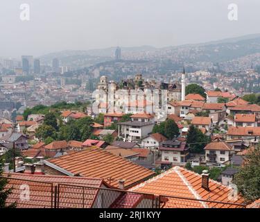 Erhöhter Blick über die Dächer in Sarajevo, Bosnien und Herzegowina, 19. August 2023. Großes Herrenhaus mit beschädigtem Dach auf dem Hügel. Stockfoto
