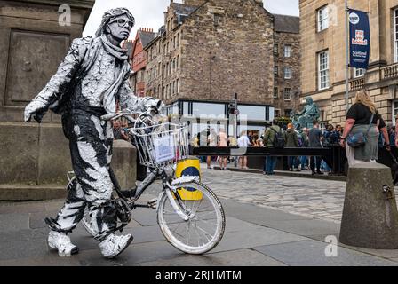 Edinburgh, Schottland, Großbritannien, 20. August 2023. Straßenkünstler in Fringe: Eine lebendige bemalte Statue auf der Royal Mile mit einem Fahrrad. Sally Anderson/Alamy Live News Stockfoto