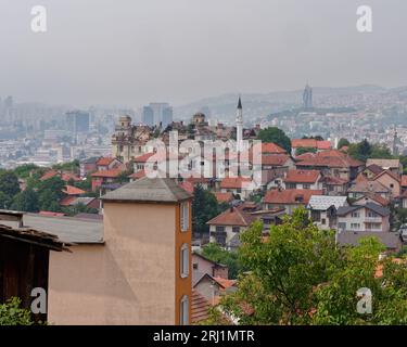 Erhöhter Blick über die Dächer in Sarajevo, Bosnien und Herzegowina, 19. August 2023. Gebäude mit beschädigtem Dachzentrum und Avaz Twist Tower dahinter. Stockfoto