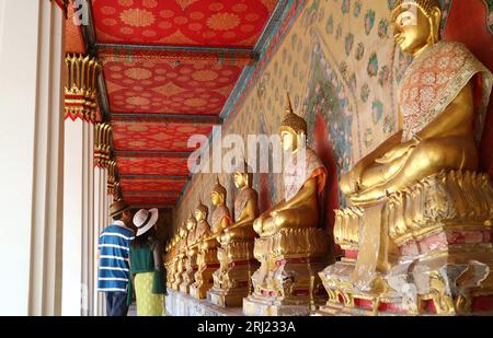 Paare im Kloster mit einer großen Gruppe von wunderschönen sitzenden Gilded Buddha-Bildern im Wat Arun oder im Tempel der Morgenröte, Bangkok, Thailand Stockfoto