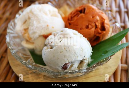 Nahaufnahme von drei Schaufeln gesüßtem Thai-Tee und Kokosnussmilch-Eis in einer Glasschale Stockfoto