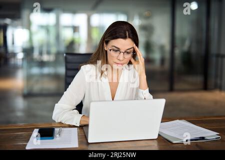 Müde, besorgte, reife Geschäftsfrau, die eine Brille trägt und Kopfschmerzen bei der Arbeit hat. Stockfoto