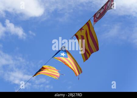 Die Flaggen von Katalonien hängen an einem Kabel und entwickeln sich im Wind gegen den blauen Himmel in den Sonnenstrahlen. Stockfoto