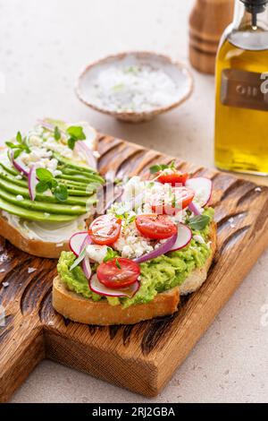 Avocado-Toasts mit Radieschen, Tomaten und Feta, garniert mit Olivenöl, gesunde Frühstücksidee Stockfoto