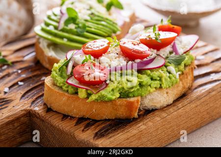 Avocado-Toasts mit Radieschen, Tomaten und Feta, garniert mit Olivenöl, gesunde Frühstücksidee Stockfoto