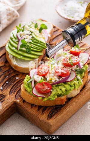 Avocado-Toasts mit Radieschen, Tomaten und Feta, garniert mit Olivenöl, gesunde Frühstücksidee Stockfoto