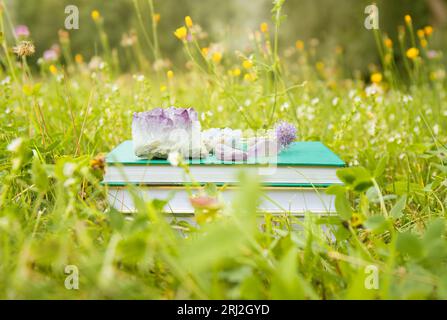 Selbsthilfe oder esoterische Themenbücher im Stapel mit Kristallgeoden im Freien an sonnigen Sommertagen mit blokeh Natur Wiesengarten im Hintergrund. Stockfoto