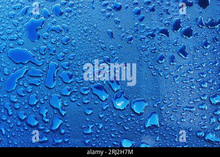 Wassertropfen mit Lichtreflexion auf blauer Kunststoffoberfläche als Hintergrund, Draufsicht Stockfoto