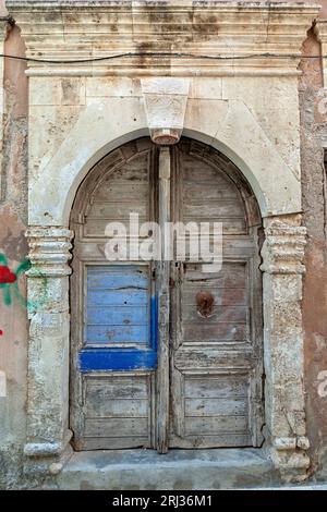 Alte Wetter Holztür mit Steinbogen Sturz in einem verlassenen alten Herrenhaus in der Altstadt von Rethymno, auf der Insel Kreta, Griechenland, Europa. Stockfoto