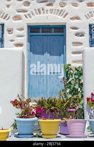 Bunte Blumentöpfe vor einem traditionellen Steinhaus mit hölzerner blauer Tür auf der Insel Koufonisi, auf den Kykladen, Griechenland, Europa. Stockfoto