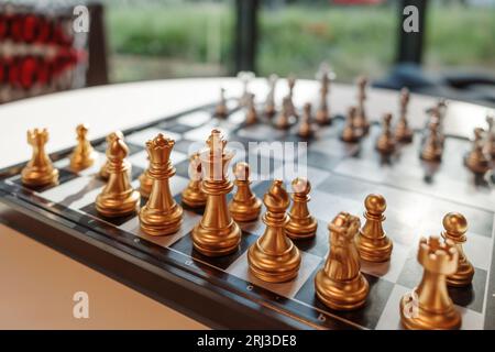 Selektiver Fokus auf die goldenen Stücke des Königs stehen und mit anderen Teilen auf Schachbrett gegen silberne Stücke im unscharfen Innenraum gesetzt. Stockfoto