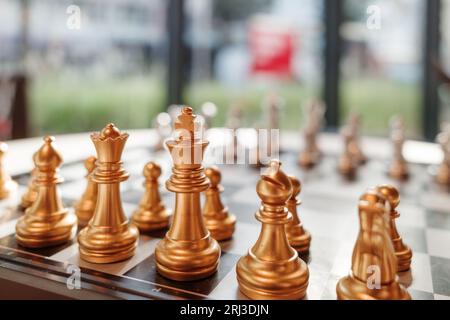 Selektiver Fokus auf die goldenen Stücke des Königs stehen und mit anderen Teilen auf Schachbrett gegen silberne Stücke im unscharfen Innenraum gesetzt. Stockfoto