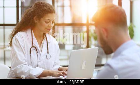 Schöne Ärztin, die ein Röntgenbild hält und anschaut, während sie es mit dem Patienten diskutiert Stockfoto