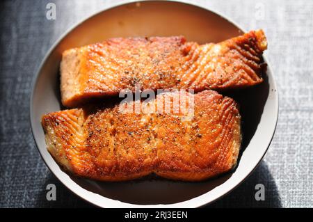 Ein Nahaufnahme eines gekochten Lachsfilet, gewürzt mit Kräutern und Gewürzen, serviert in einer weißen Schüssel auf einer Holzoberfläche Stockfoto