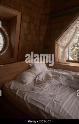 Ein modernes Schlafzimmer mit einem komfortablen Bett mit weißen Laken und Kissen und einem Fenster für natürliches Licht Stockfoto