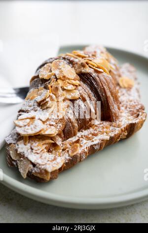 Eine Nahaufnahme eines Mandel-Croissants auf einem Teller mit weißem Puderzucker, der darauf bestreut ist Stockfoto