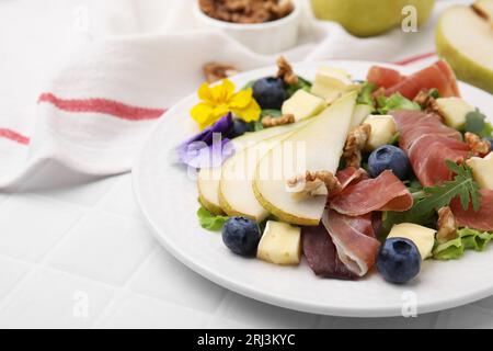 Leckerer Salat mit Brie-Käse, Prosciutto, Walnüssen und Birne auf weißem Kacheltisch, Nahaufnahme. Leerzeichen für Text Stockfoto
