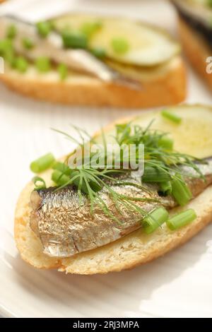 Köstliches Sandwich mit Sprotte, eingelegter Gurke, grüner Zwiebel und Dill auf dem Teller, Nahaufnahme Stockfoto