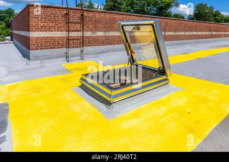 Dachluke für den Zugang zum Dach mit eingebautem Oberlicht auf einem Spritzschaumdach mit lackiertem gelbem Gehweg Stockfoto