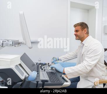 Männlicher Ultraschalltechniker, der für eine Patientin in der medizinischen Klinik Ultraschalluntersuchungen des Abdomens durchführt Stockfoto
