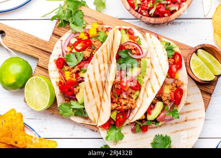 Mexikanische Küche. Tacos mit Rindfleisch, Mais, roten Bohnen, Tomatensalsa-Sauce und Zwiebeln in Maistortilla an Bord. Weißer Tischhintergrund, Draufsicht Stockfoto