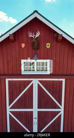 Außenansicht einer rot-weißen Scheune mit montiertem Hirschkopf Stockfoto