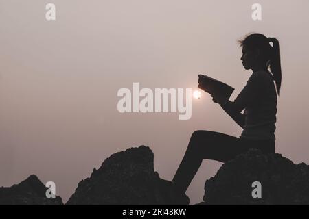 Frauen, die die heilige Bibel halten, um Gott bei Sonnenuntergang zu verehren, beten zum Gott, christliches Silhouettenkonzept. Stockfoto
