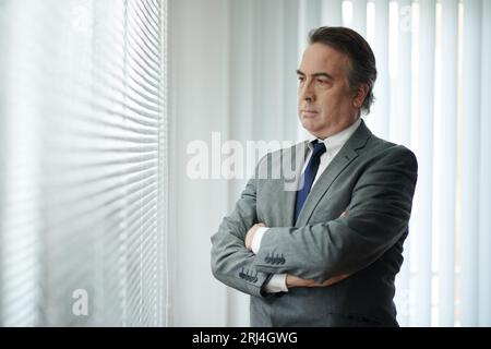Porträt eines Reifen Geschäftsmannes in grauem Anzug, der die Arme kreuzt und wegschaut Stockfoto