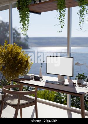 Ein moderner, tropischer, luxuriöser Büroarbeitsplatz vor dem Glasfenster mit atemberaubendem Meerblick, einem weißen Computerbildschirm auf einem Tisch und einem Housepla Stockfoto