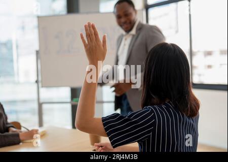 Nahaufnahme einer asiatischen Geschäftsfrau, die während des Meetings die Hand hebt, eine Frage stellt oder eine Frage beantwortet. Stockfoto