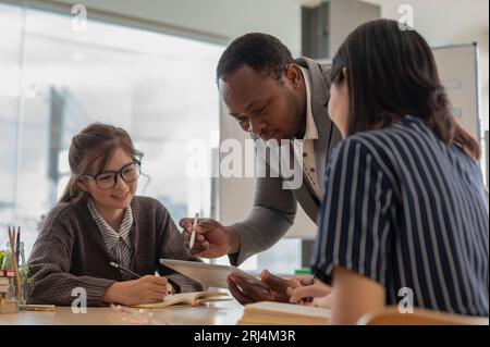 Ein professioneller afroamerikanischer Geschäftsmann oder männlicher Chef, der asiatische Mitarbeiter im Besprechungsraum, Brainstorming und Briefing-Projekt ausbildet. Vielfältiger Bus Stockfoto