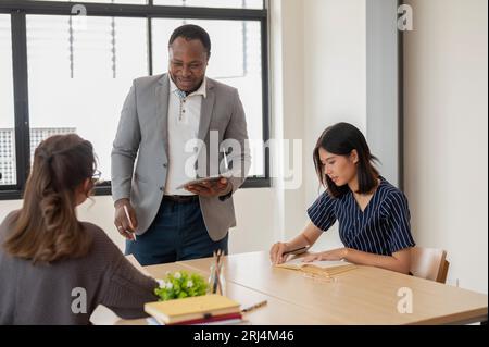 Ein afroamerikanischer Englischlehrer oder -Tutor gibt asiatischen Schülern während des Unterrichts Hausaufgaben. Bildung, multirassisches Umweltkonzept Stockfoto