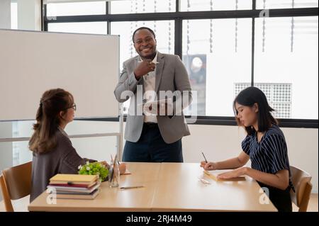 Ein glücklicher afroamerikanischer Englischlehrer oder -Tutor lachen und genießt es, asiatische Schüler in der Klasse an einer Sprachschule zu unterrichten. Bildung und Mu Stockfoto