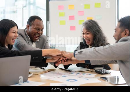 Eine multirassische Gruppe fröhlicher und erfolgreicher Geschäftsleute trifft sich in einem Meeting, setzt sich als Team zusammen und feiert ihr erfolgreiches Projekt Stockfoto