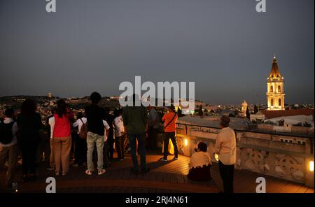 Touristen genießen den Blick auf die Altstadt mit dem beleuchteten Uhrturm des Klosters des Heiligen Erlösers. Jerusalem, Israel. Stockfoto