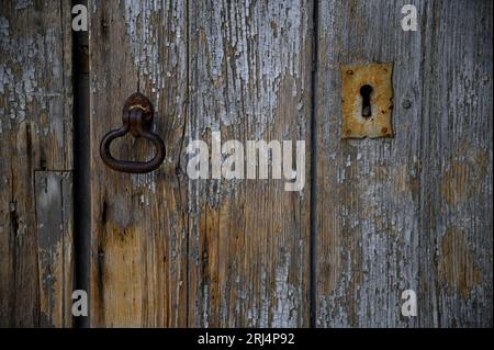 Antike graue Holztür mit rostigem Schlüsselloch und schmiedeeisernem Klopfer in Scicli Sicily, Italien. Stockfoto