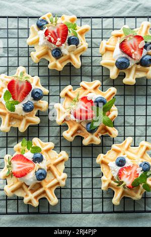 Frisch gebackene Waffeln mit Erdbeeren und Blaubeeren auf Textilhintergrund. Hausgemachtes Backen. Stockfoto