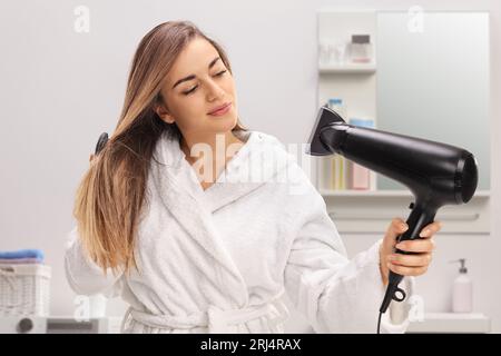 Mädchen im Bademantel bläst ihr Haar mit einem Haartrockner im Badezimmer Stockfoto